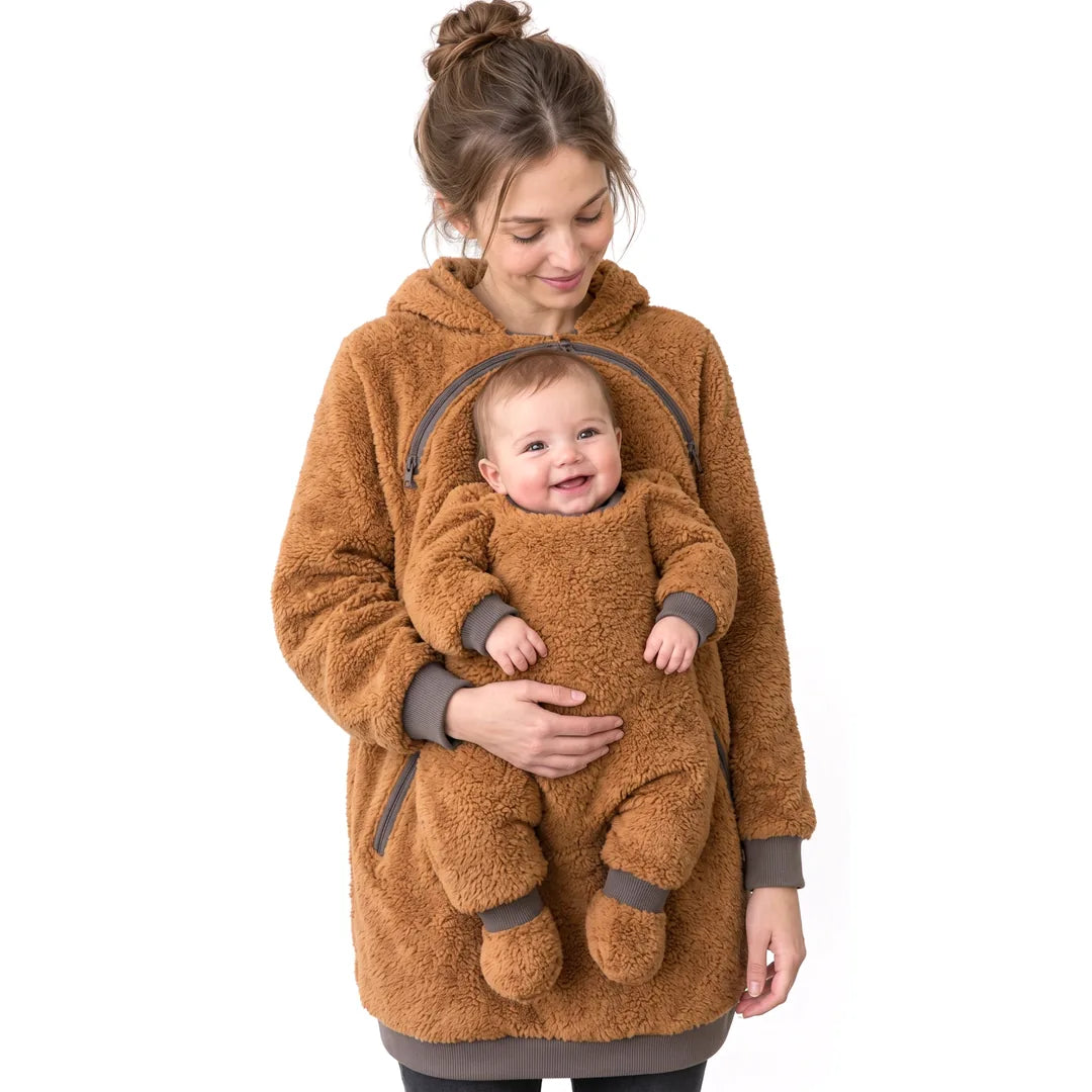 Mother wearing a camel brown fleece babywearing hoodie with infant positioned at the front and supported by her hand